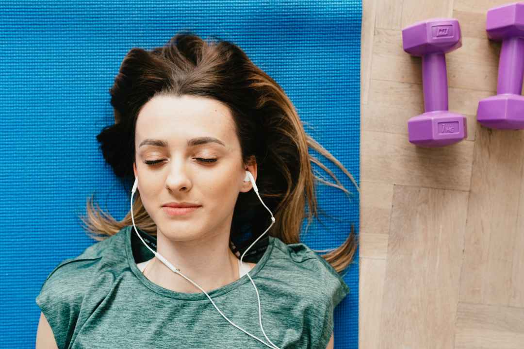 woman listening to music in earphones while resting after home workout